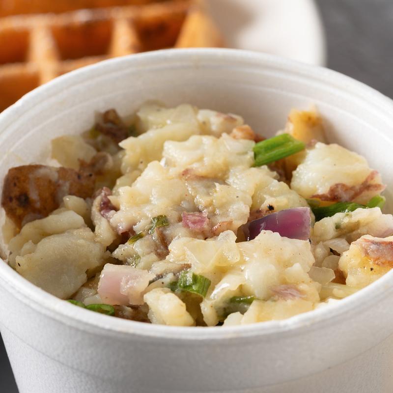 A side of heavenly potatoes with red onion and green onion beside a waffle