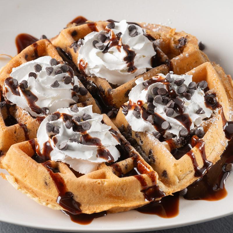 Belgian waffle topped with whipped cream, chocolate chips and chocolate drizzle