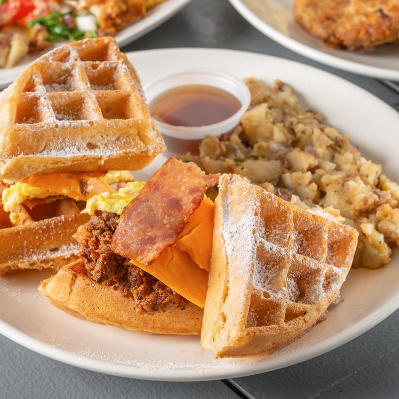 Chicken and waffle sandwich with bacon, cheese and breakfast potatoes
